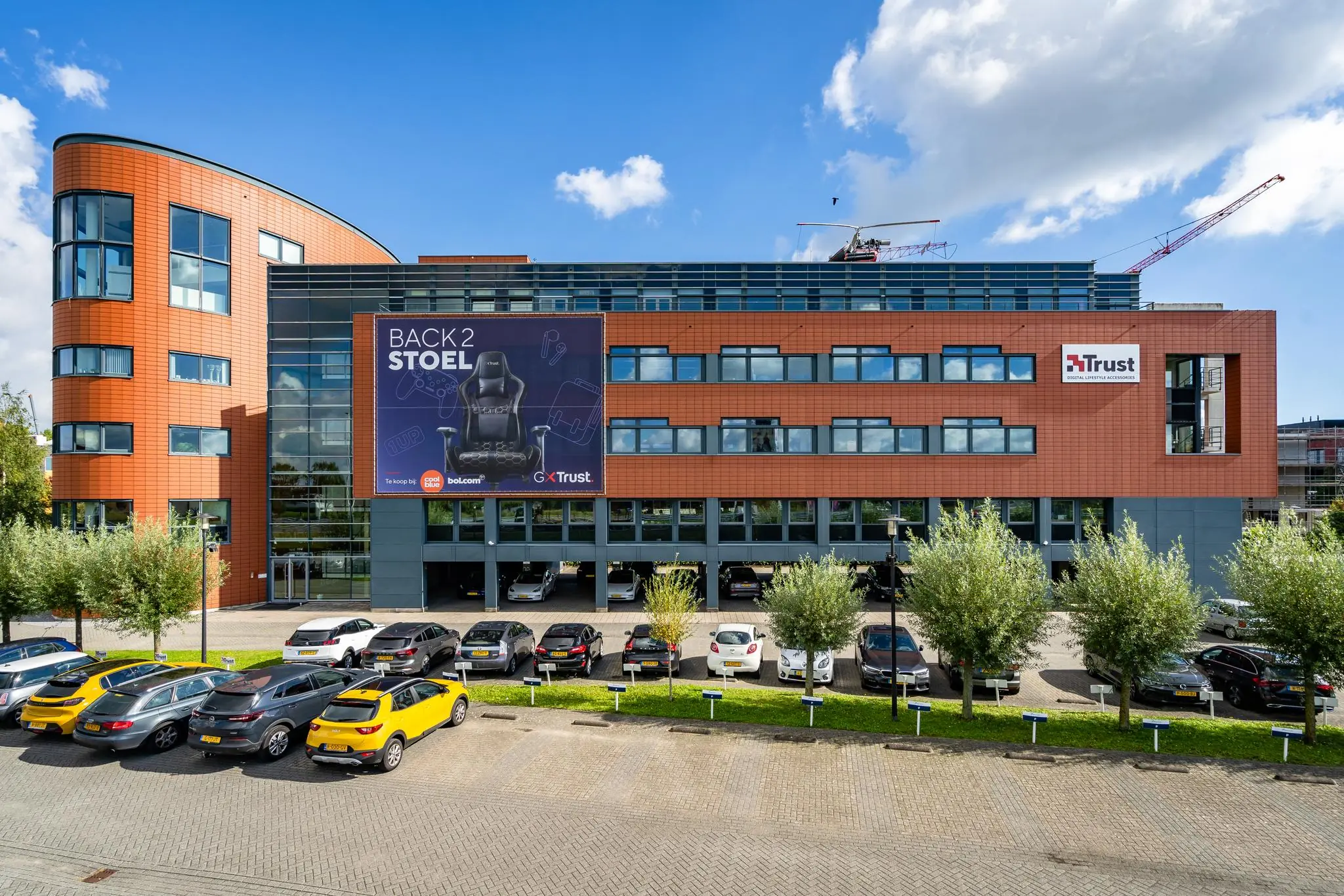 Modern kantoorgebouw aan de Laan van Barcelona met een groot reclamebord van Trust en geparkeerde auto's op de voorgrond.